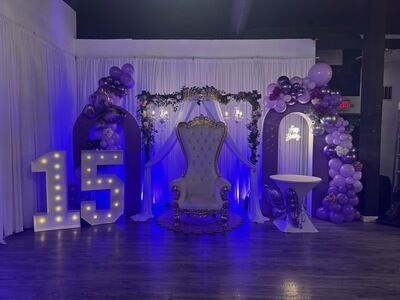 Quinceañera venue setup with 15 marquee lights, purple and blue mood lighting, and throne chair