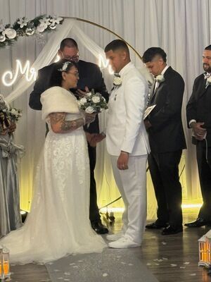 Bride and groom exchanging vows at The Prestige Venue under gold arch with officiant