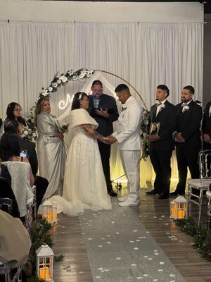 Wedding ceremony at The Prestige Venue with gold arch, Mr and Mrs neon sign, white drapes, and bridal party